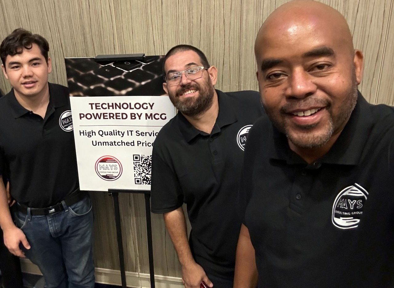 Four members of the MCG team in black MCG polos next to a sign reading Technology Powered by MCG